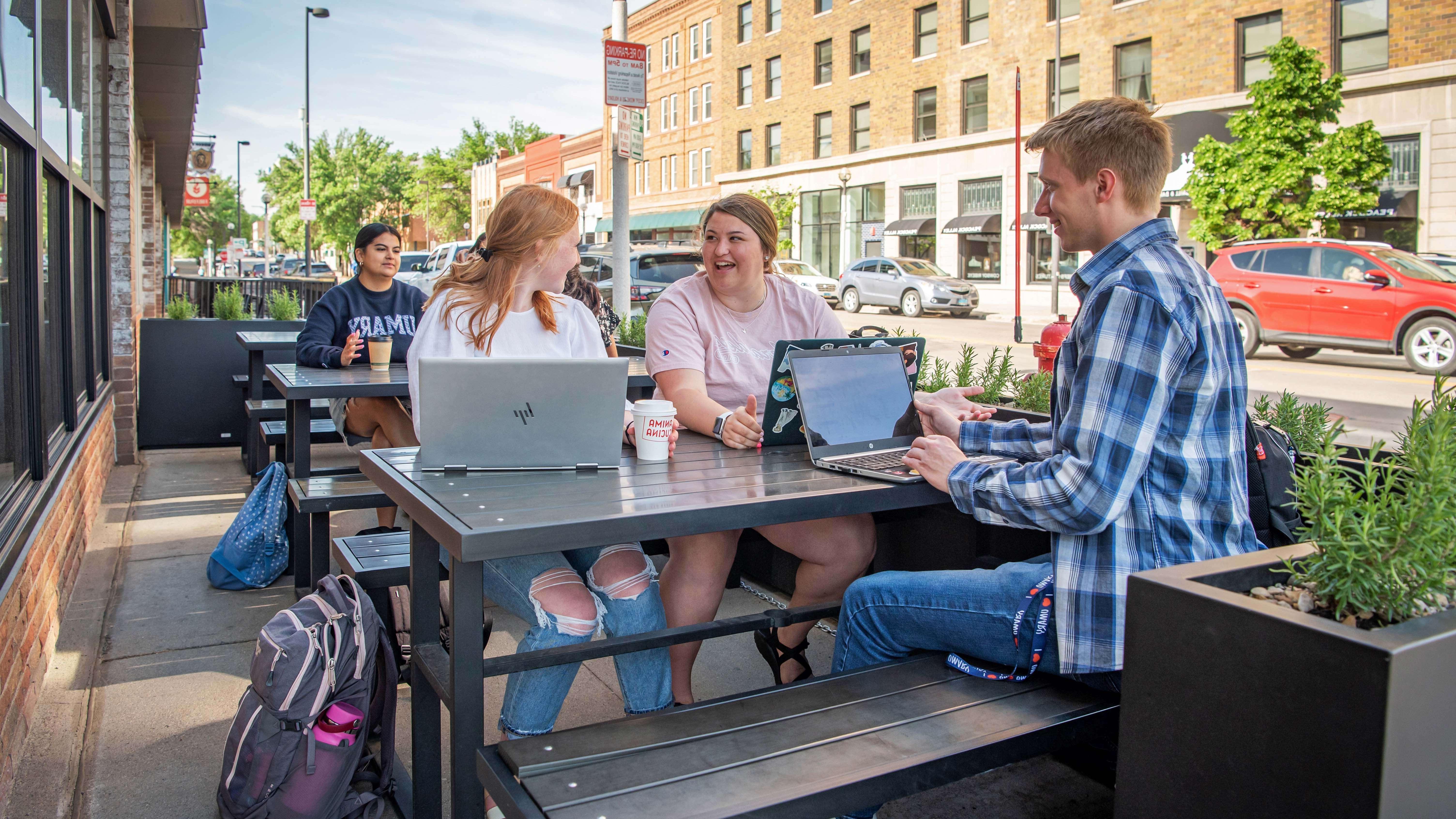 Three University of Mary students sitting at picnic table outside a restaurant in downtown Bismarck